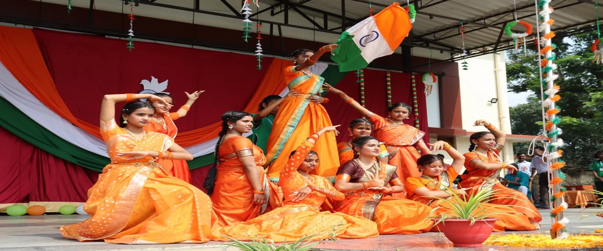 Girls of the school in orange saris performing a dance on a stage decorated in the colours of the Indian flag